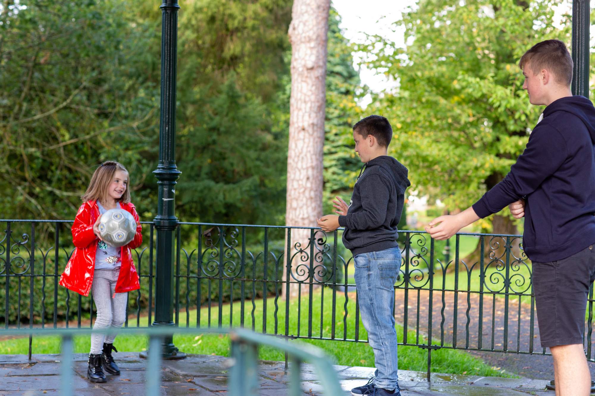 Three siblings throwing a ball to each other in the park